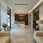 Reception area interior design - https://www.andyquinones.net Httpswww Andyquinones Net spa reception with white leather couches marble floor and a wood paneled back wall featuring the rejuv chip logo behind the desk